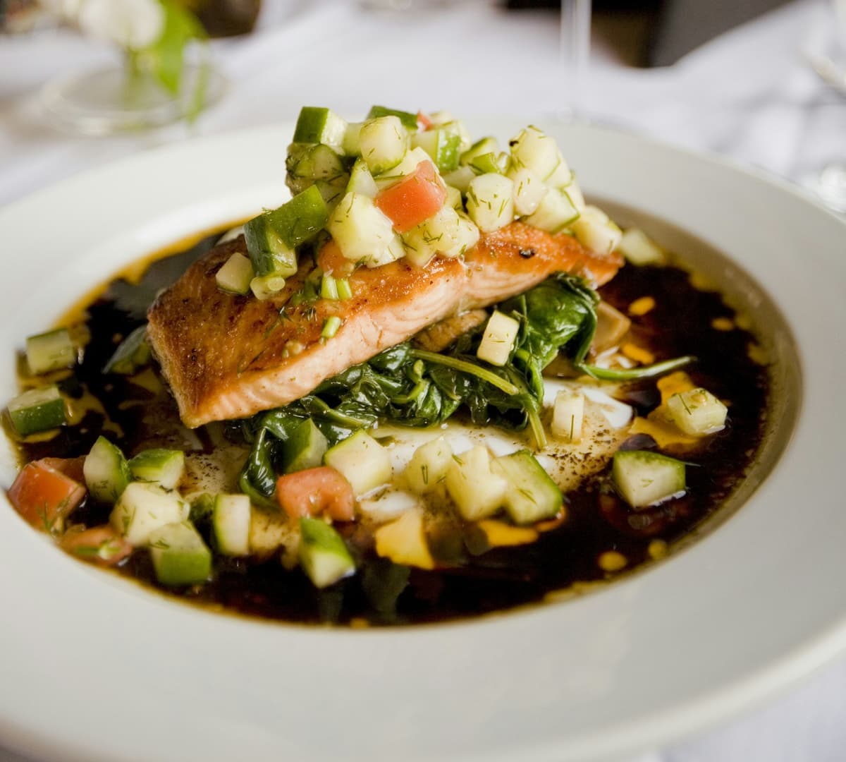 A plated salmon fillet with sautéed greens and fresh salsa at a restaurant table